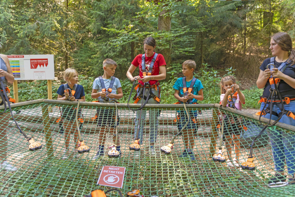 Eine Kletterwald Mitarbeitern gibt Kindern eine Sicherheitseinweisung, bevor diese im Kletterwald klettern dürfen.