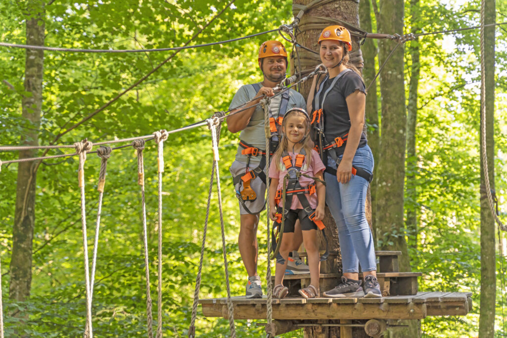 Eine Famile steht auf einer Plattform in einem Kletterwald Parcours und lächelt direkt in die Kamera.