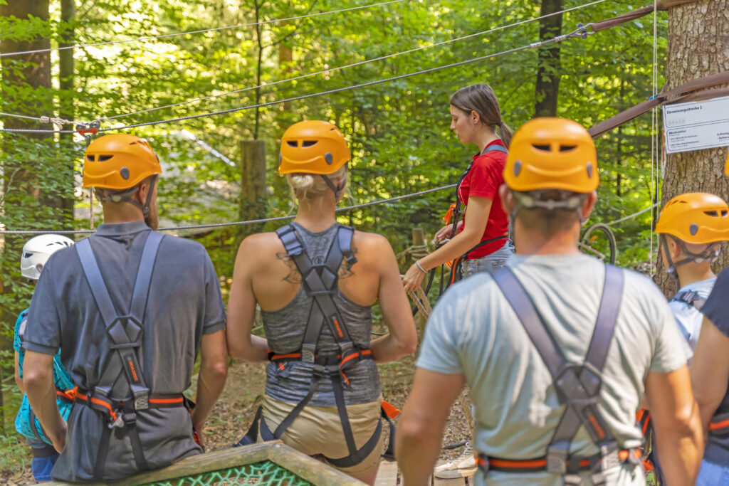 Eine Gruppe bekommt gerade eine Sicherheitseinweisung von einer Mitarbeiterin des Kletterwald Prien am Chiemsee.