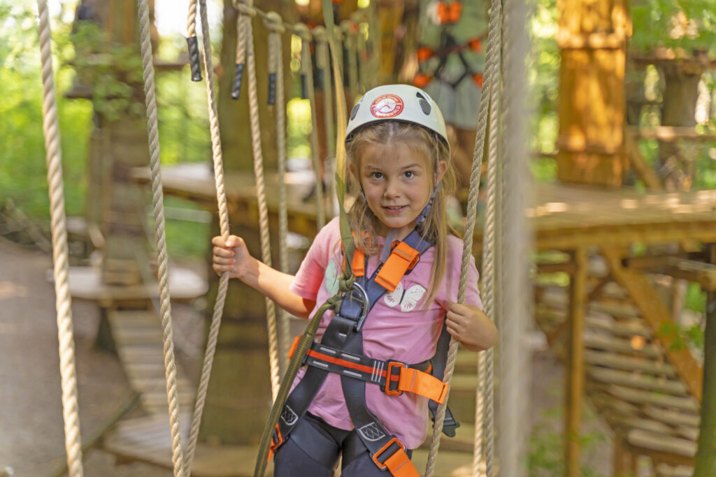 Ein Mädchen mit Helm und Klettergurt steht in eine Parcours zwischen Seilen im Kletterwald Prien am Chiemsee.