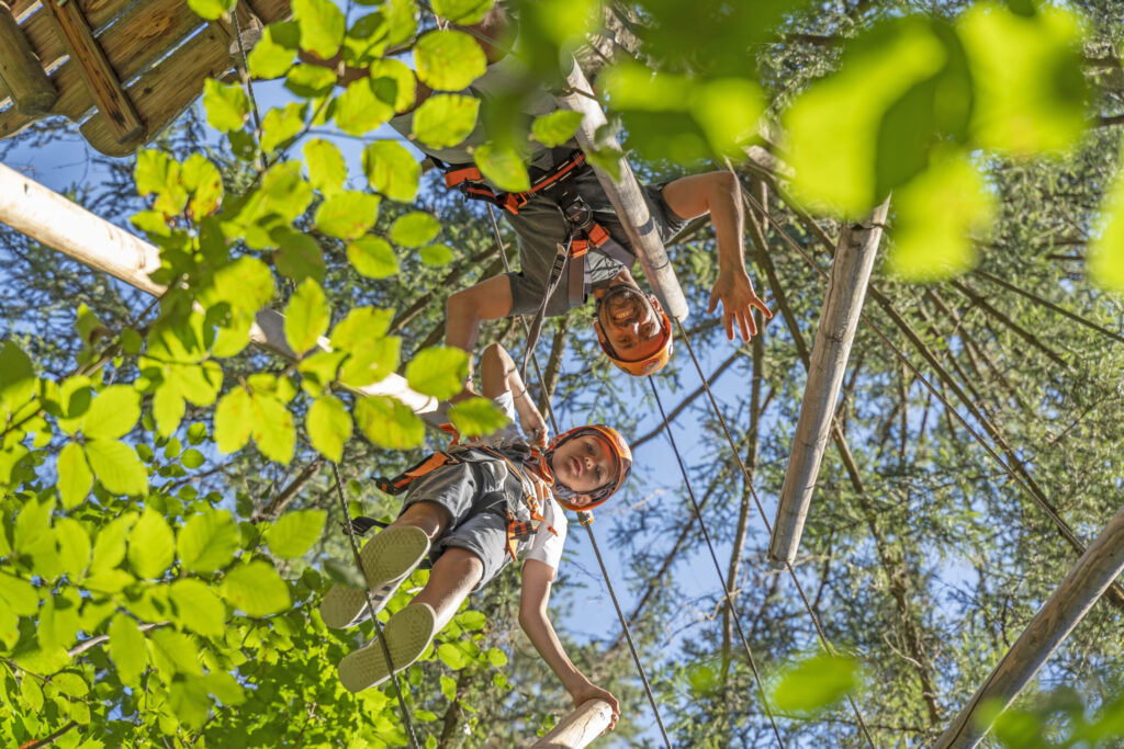 Ein Junge und sein Vater befinden sich in einem Parcours im Kletterwald Prien am Chiemsee und schauen nach unten direkt in die Kamera.
